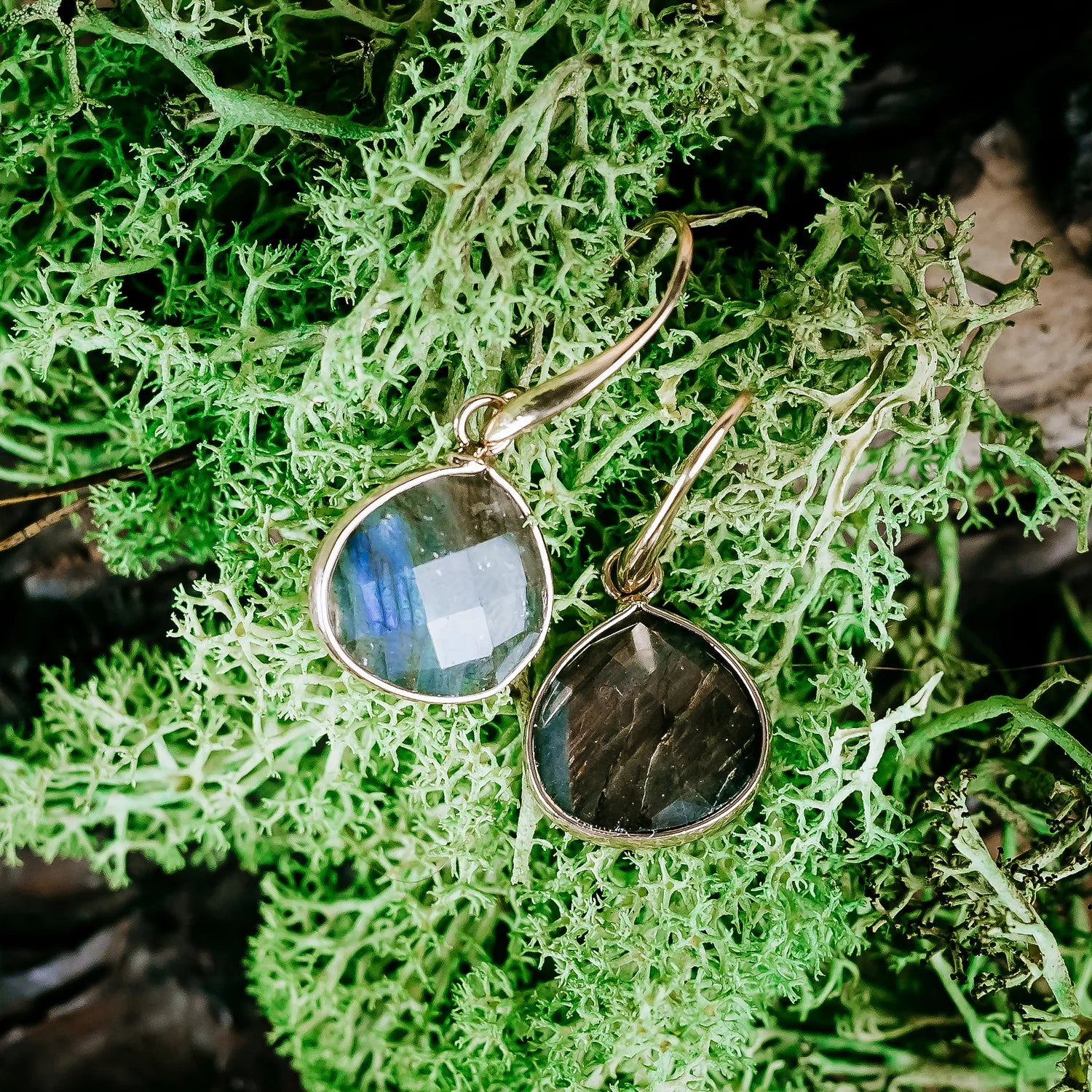 Kolczyki z labradorytem położone na zielonym mchu.