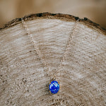 Naszyjnik z opalem symbolizującym spokój zawieszony na plastrze drewna.