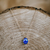 Naszyjnik z opalem symbolizującym spokój zawieszony na plastrze drewna.